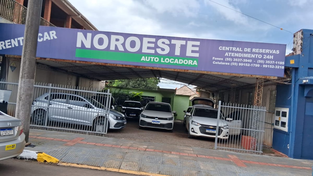 Fachada da Noroeste Auto Locadora na Rua Uruguai, com a placa azul e verde sobre o pátio coberto onde ficam os carros.