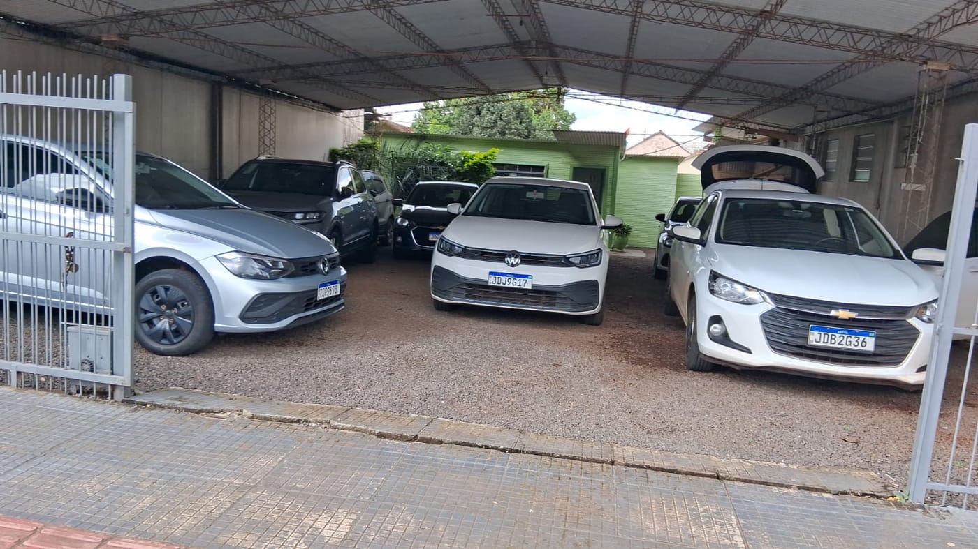 Pátio coberto da locadora com hatches e sedans compactos brancos e prata estacionados lado a lado.